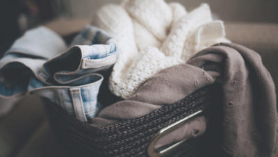 Basket on top of bed holding jeans, sweatshirt, and sweater